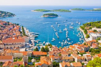 Aerial view of town with red roofs overlooking the blue sea with white sailing boats and small green islands in the distance