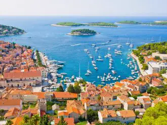 Aerial view of town with red roofs overlooking the blue sea with white sailing boats and small green islands in the distance