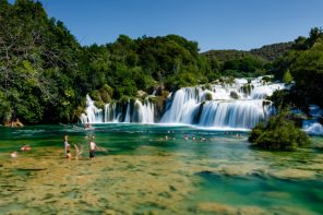 waterfall with people swimming beneath the falls