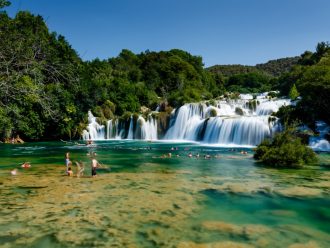 waterfall with people swimming beneath the falls