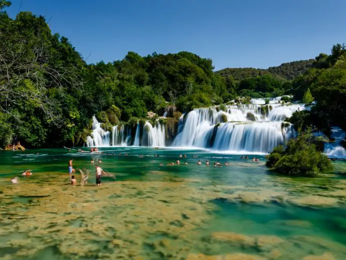 waterfall with people swimming beneath the falls