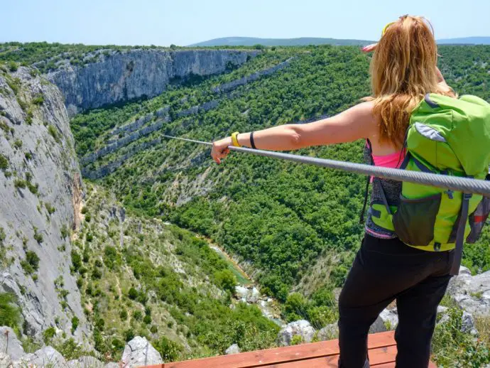 Female tourist standing on a platform looking down a zipline that goes out over a side mountainous valley