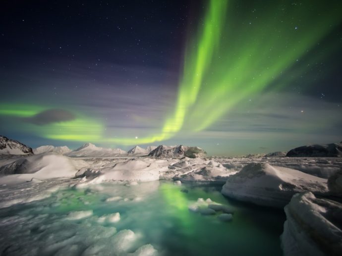Northern lights in the sky over water with small icebergs