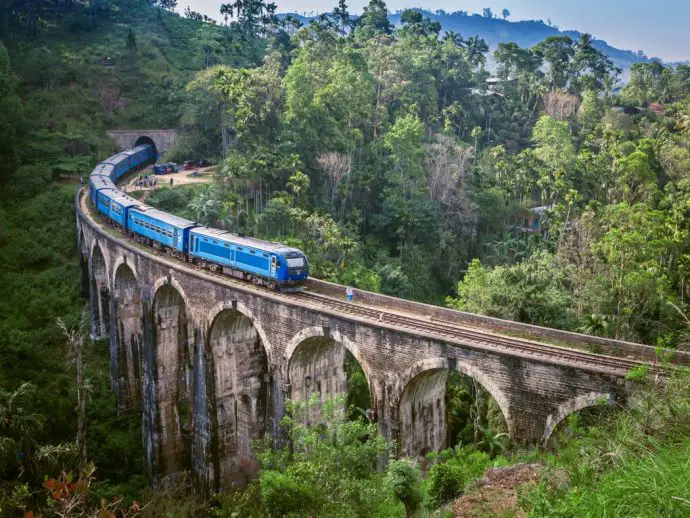 Blue train on an arched bridge travelling through lush green mountains