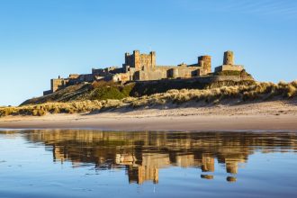 Sea in foreground looking back towards land with a long sandy beach and large castle behind