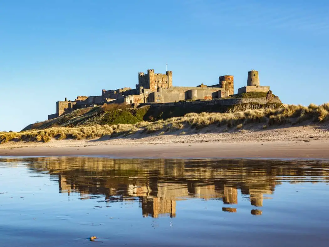 Sea in foreground looking back towards land with a long sandy beach and large castle behind