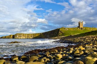 Sea to left, rocky foreground to right, with distant green cliffs and a castle ruin on top