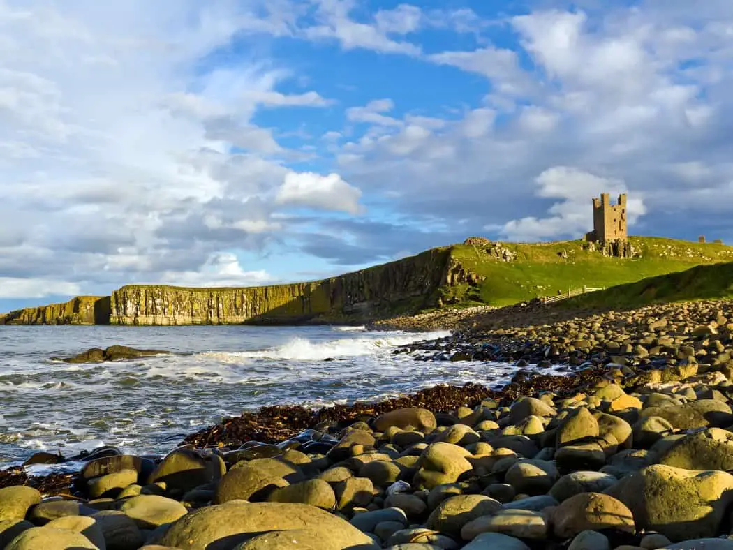 Sea to left, rocky foreground to right, with distant green cliffs and a castle ruin on top