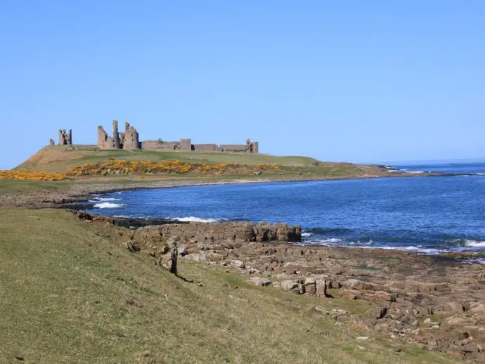 Green fields with ocean to the right, and a castle ahead on a rocky headland
