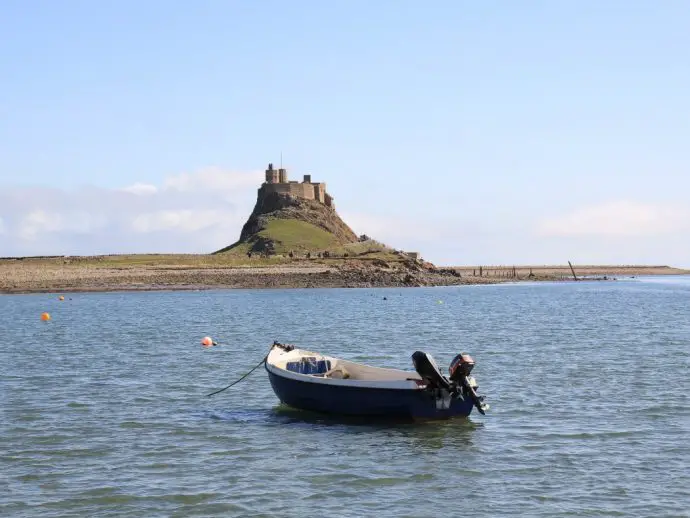 Sea with fishing boat in foreground and a small island with a castle on top in the background