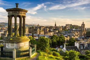 Edinburgh skyline with blue sky and a stone monument in the foreground