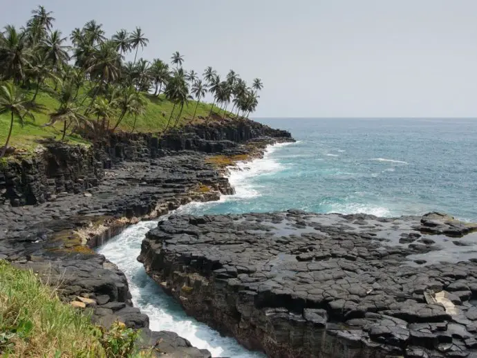 Black volcanic shore with palm trees beside the sea - Boca do Inferno on Sao Tome