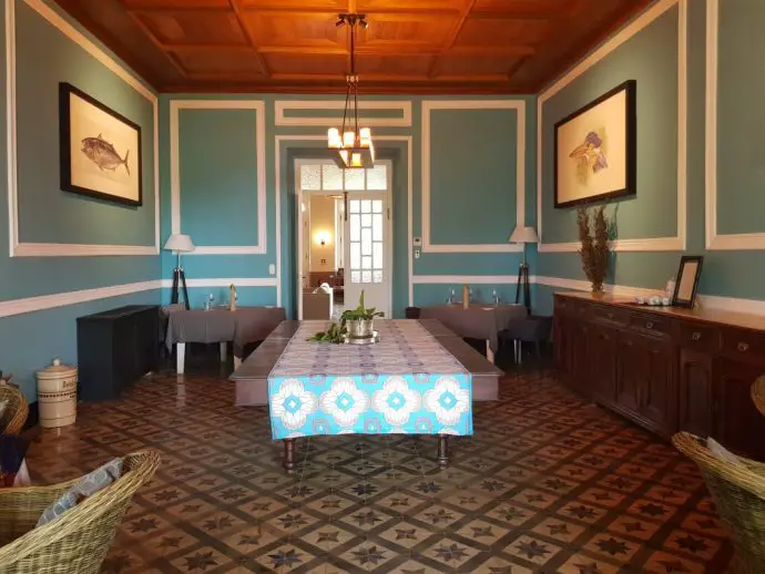 Large open colonial style dining room at Sundy Roca on Principe with teal coloured walls, tiled floor and wooden ceiling