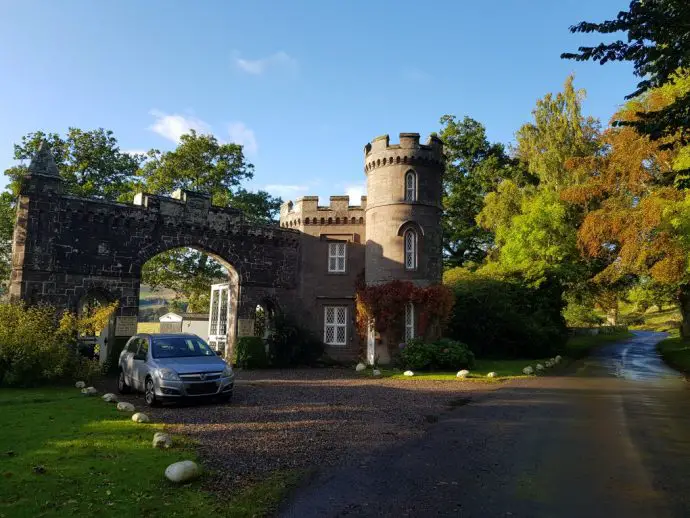 Castle gatehouse by the side of a road surrounded by green trees