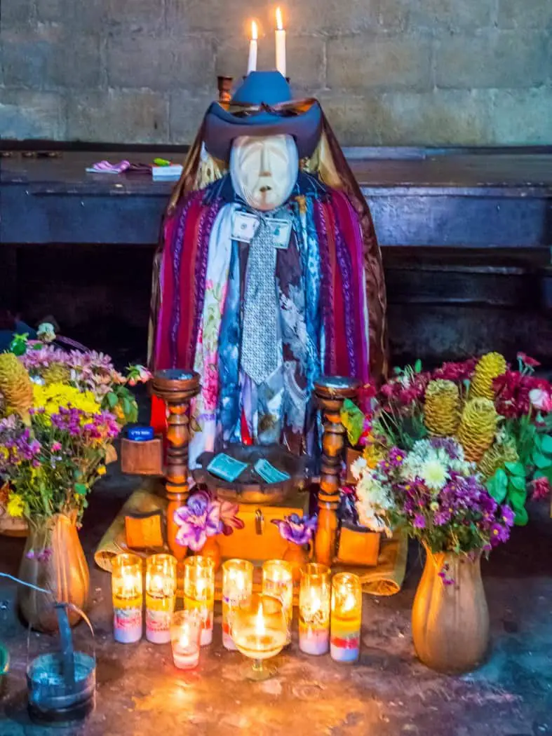 colourful wooden effigy of a saint surrounded by candles
