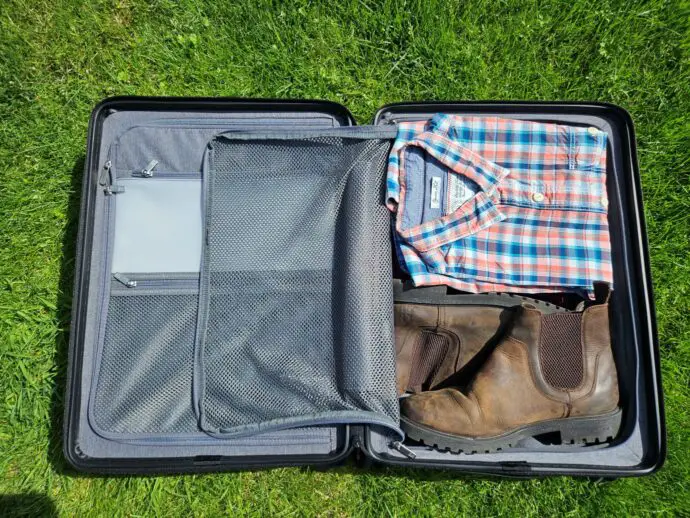 Open suitcase with zipped compartments containing clothes and shoes