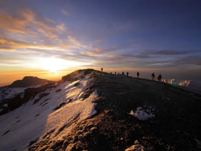 People climbing up a mountain in the dark with the sunrise in the distance
