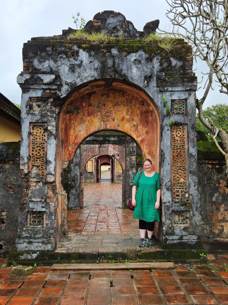 Woman in a green dress standing in front of an old stone gateway